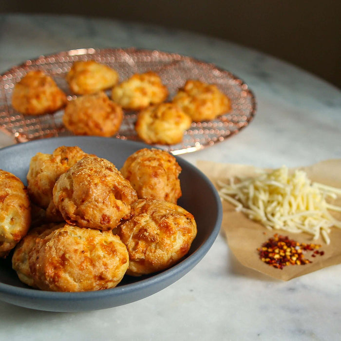 Delicious Red Pepper Gougeres Recipe served in a bowl with a plate of more gougeres and cheese on the side.