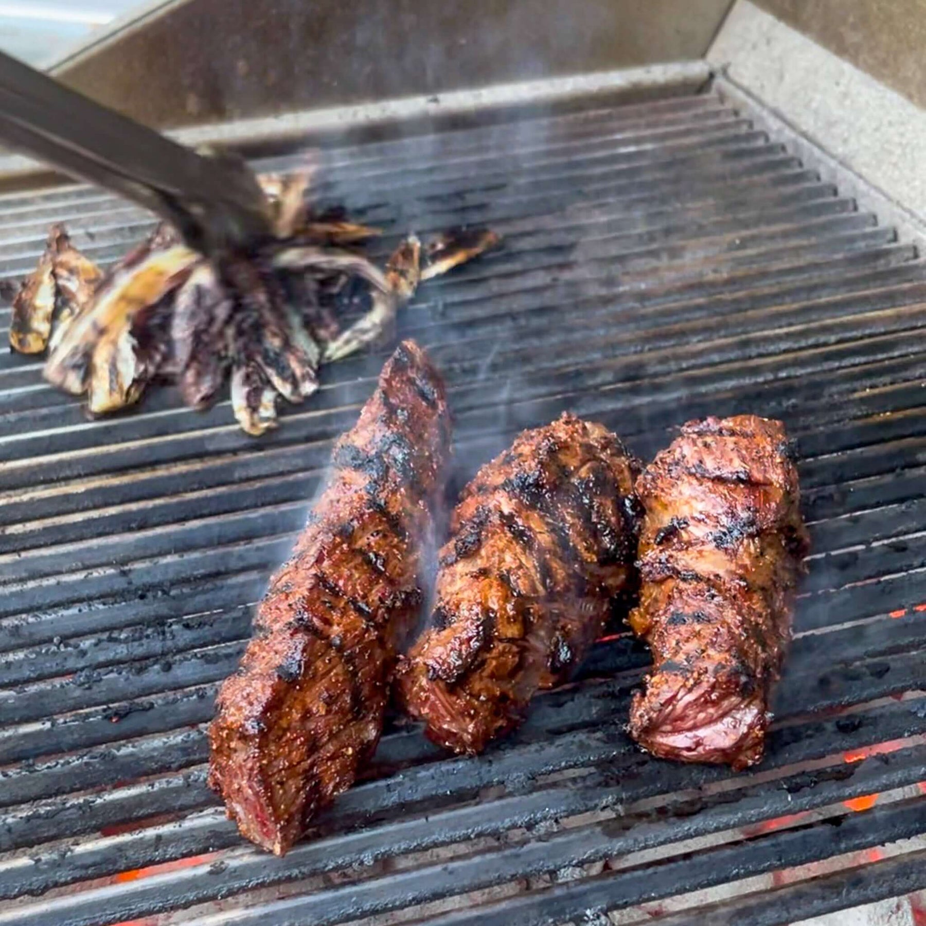 Summer Grilling Tips: juicy steaks sizzle on the grill with smoke rising in the background.