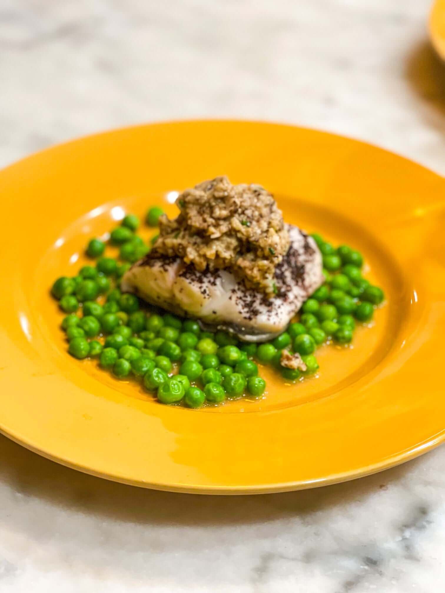 Springy Black Cod Recipe served with green peas on an orange plate, showcasing a delicious seafood dish.