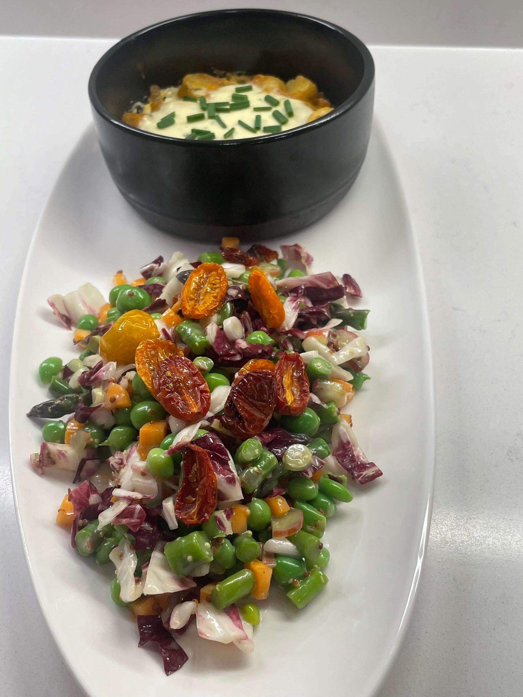 Colorful vegetarian spring dinner recipe featuring fresh vegetables and a baked dish in a black bowl.