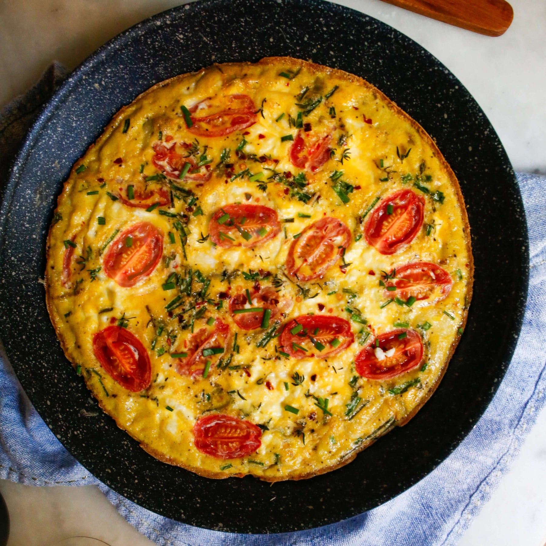 Delicious Goat Cheese Frittata Recipe and Mimosa Brunch served in a black skillet, garnished with fresh tomatoes.