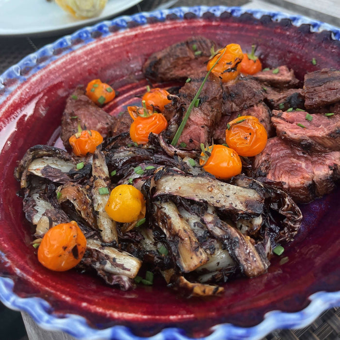 A colorful dish featuring grilled steak, charred vegetables, and tomatoes, showcasing some grilling tips.