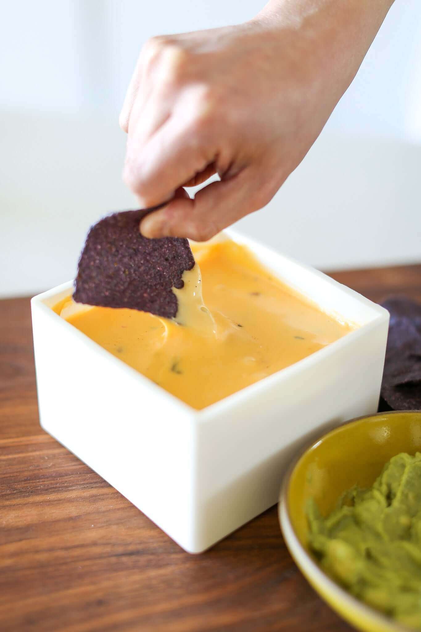 A hand dipping a purple chip into gooey queso, highlighting the delicious gooey queso recipe.