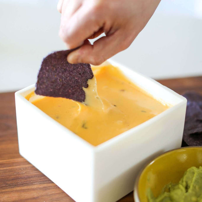 A hand dipping a purple chip into gooey queso, highlighting the delicious gooey queso recipe.