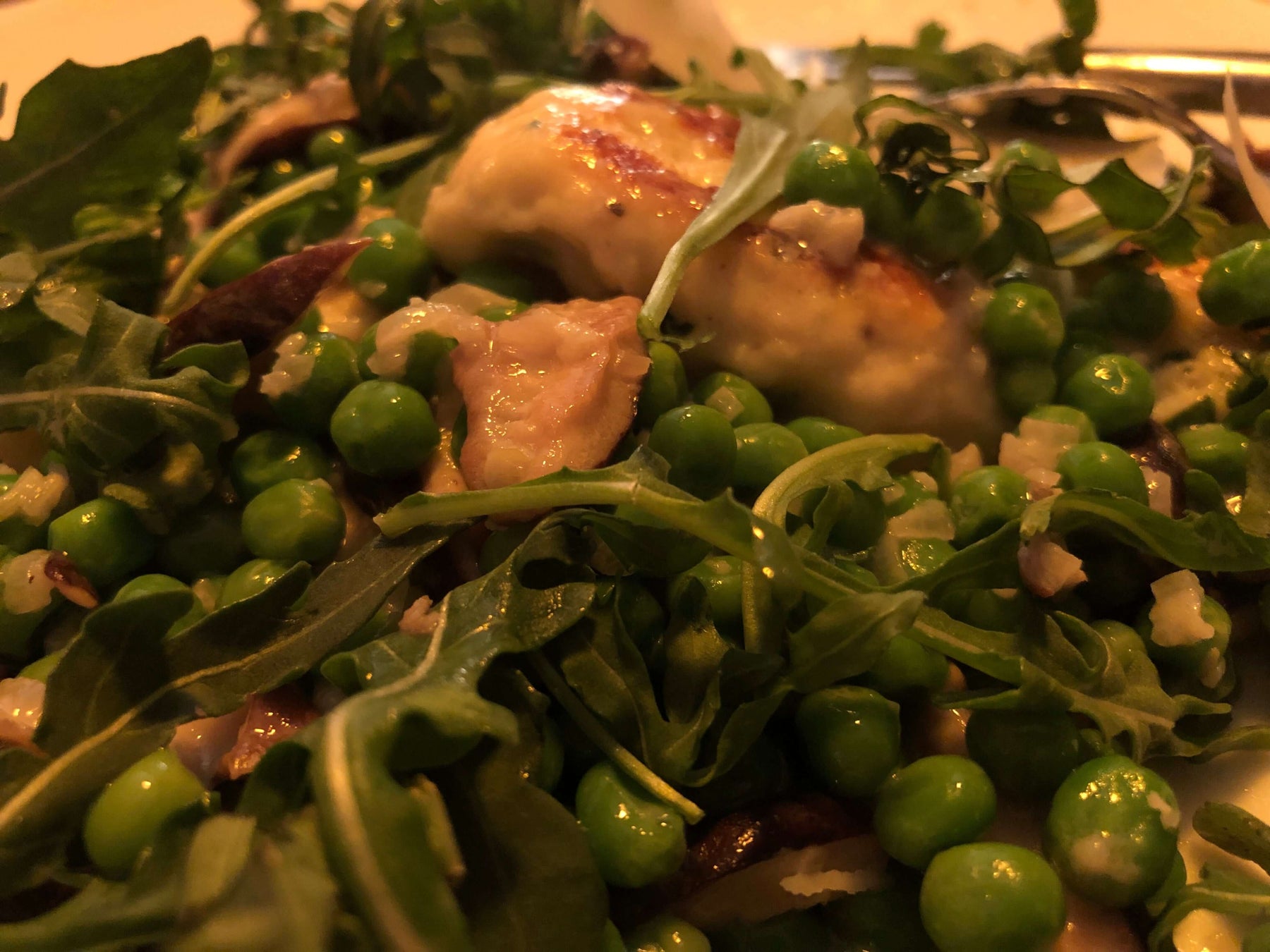 Delicious Ricotta Dumplings with Peas Recipe served on a bed of fresh greens and peas.