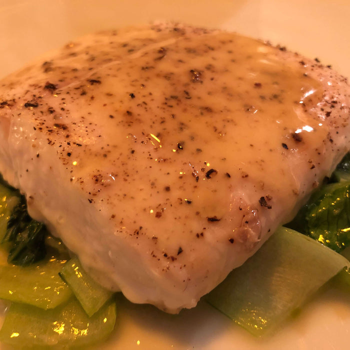 Close-up of Uncle Waltie's Quick Local Halibut Perfection topped with sauce on a bed of greens.