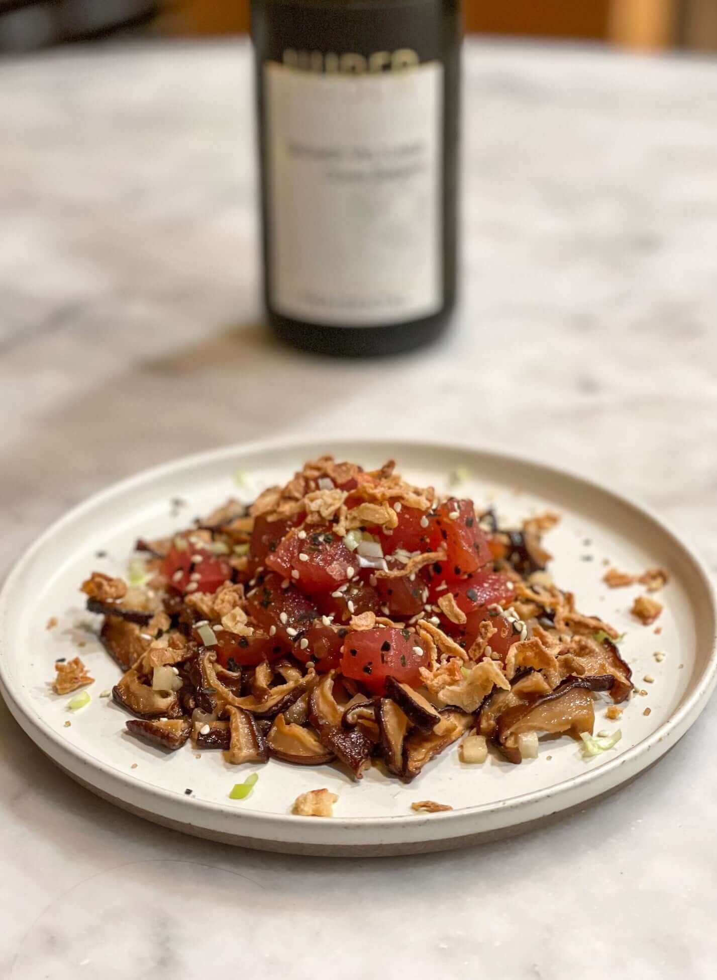 Ahi, Cepe Snack Attack Recipe served on a plate with garnishes and a bottle of wine in the background.