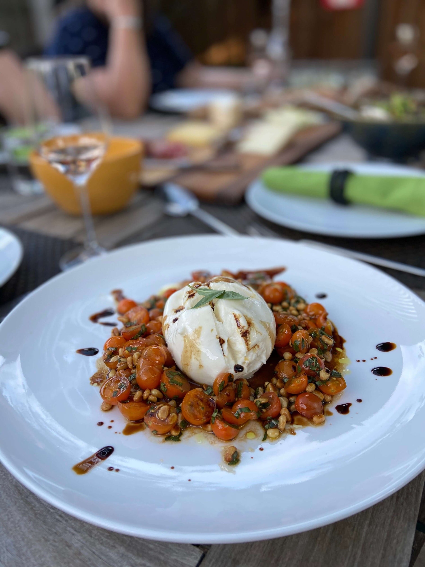 Recipe: Burrata, Cherry Tomatoes, Pine Nuts with Balsamic Drizzle served on a plate.