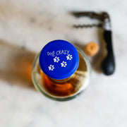 Top view of a blue silicone wine cap with paw prints, labeled 'Dog CRAZY', perfect for dog-loving wine enthusiasts.