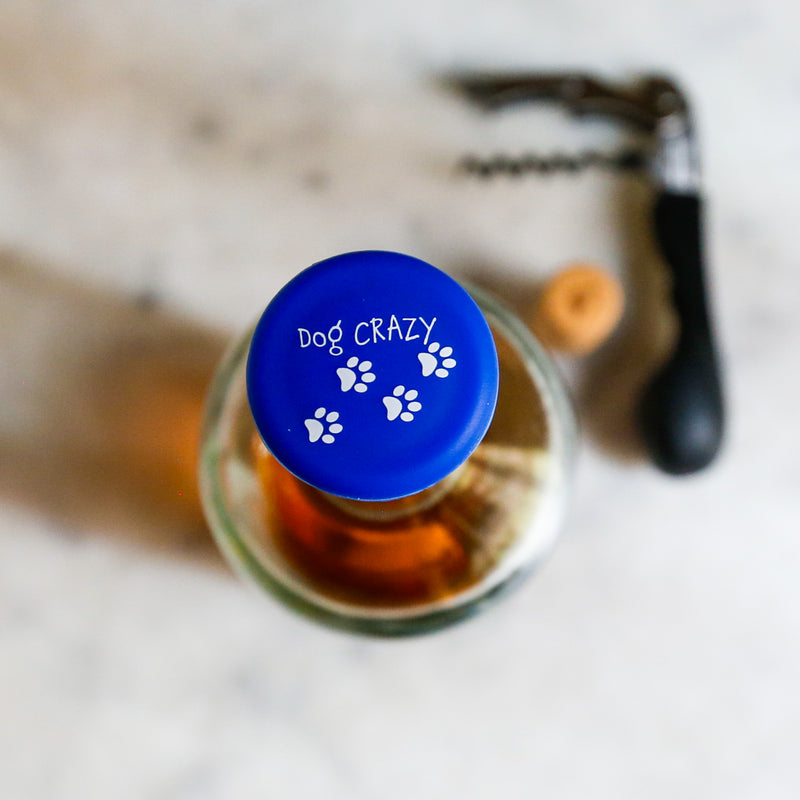Top view of a blue silicone wine cap with paw prints, labeled 'Dog CRAZY', perfect for dog-loving wine enthusiasts.