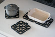 Interlocking silicone trivet protecting a pot and a dish on a modern kitchen countertop.