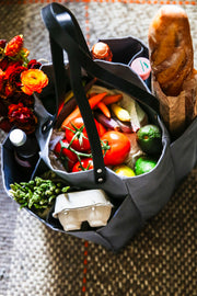 A grey multi-pocketed market tote filled with fresh vegetables, eggs, and a loaf of bread, ideal for grocery shopping.