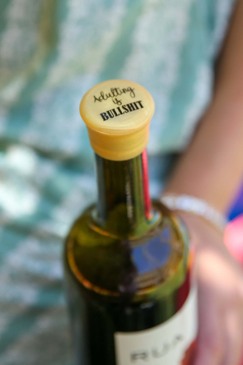 Silicone wine cap labeled 'Adulting is Bullshit' on a wine bottle, perfect for humor and adulting themed gifts.