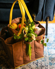 Stylish brown tote bag filled with fresh fruits and flowers, perfect for convenient shopping and home decor.
