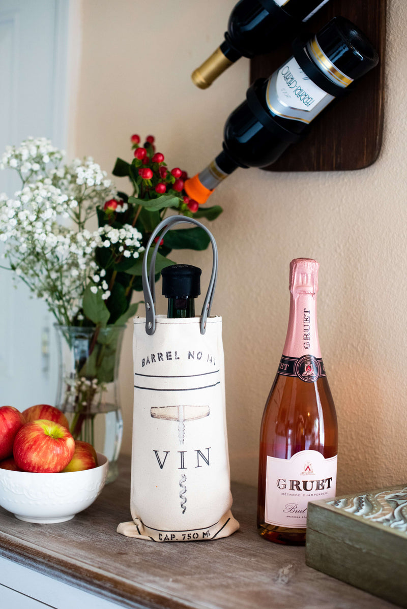 Vin Design Canvas Wine Tote displaying a wine bottle on a table with apples and flowers in a cozy setting.