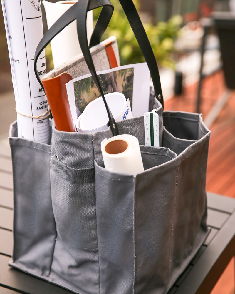 Grey multi-pocketed market tote filled with shopping items and documents on a table.