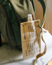 Half Full 750ml canvas canteen attached to a backpack, featuring a fun graphic design.