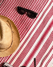 Straw hat and black sunglasses on a red and white striped beach towel.