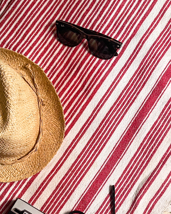 Straw hat and black sunglasses on a red and white striped beach towel.