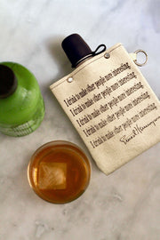 Hemmingway Quote 240ml Canvas Flask with whiskey and bottle on marble surface.