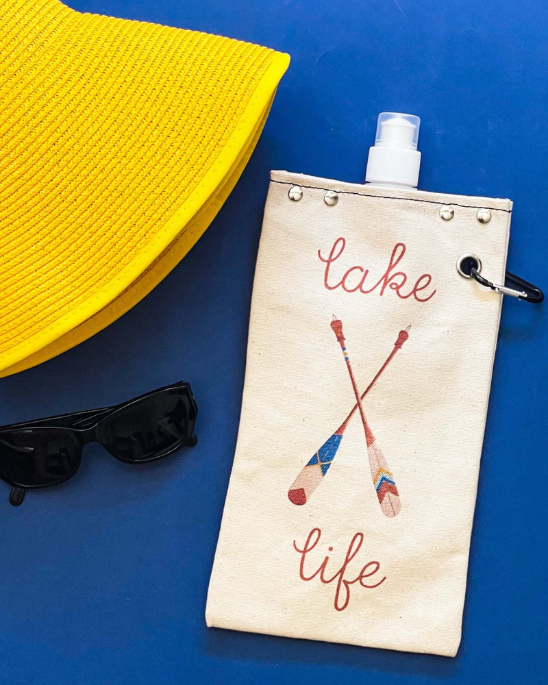 Paddle Lake canvas canteen with 'lake life' design, sunglasses, and yellow sun hat on a blue background.
