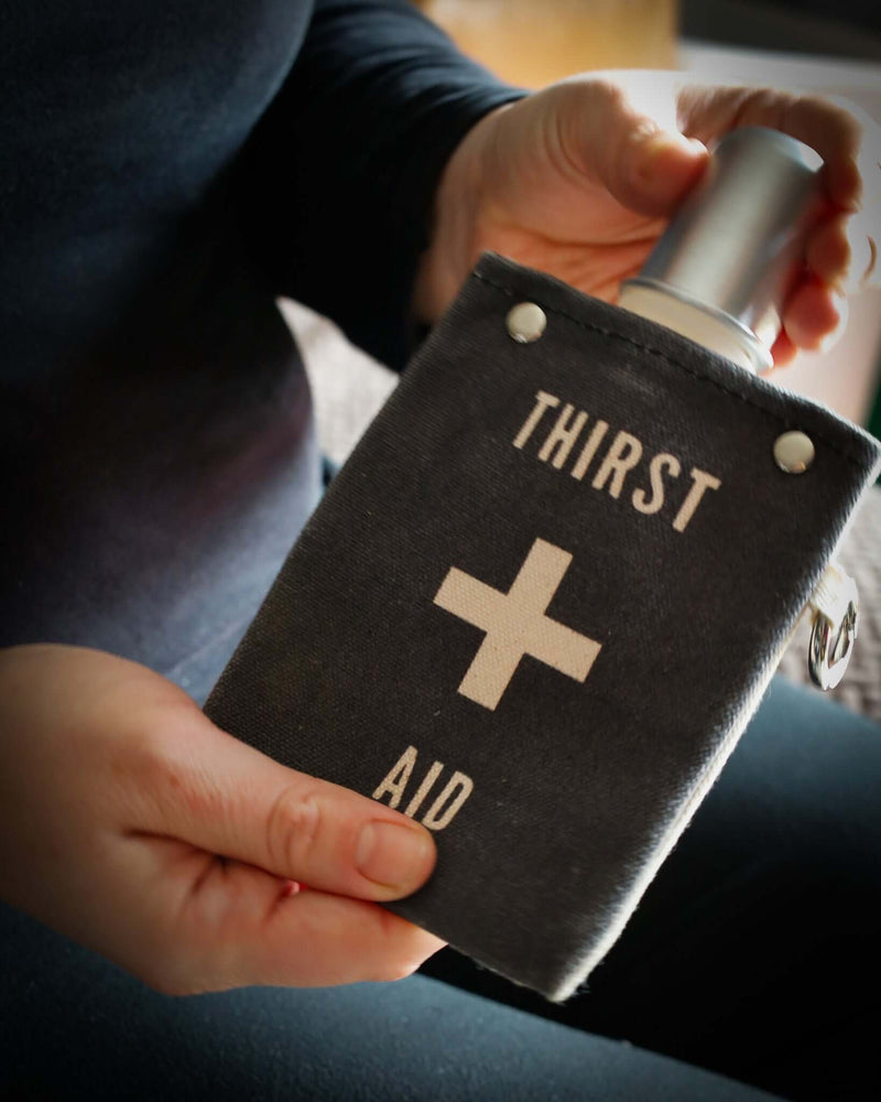 Person holding a Thirst Aid 120ml canvas flask with a BPA-free, leak-proof design and cotton cover.