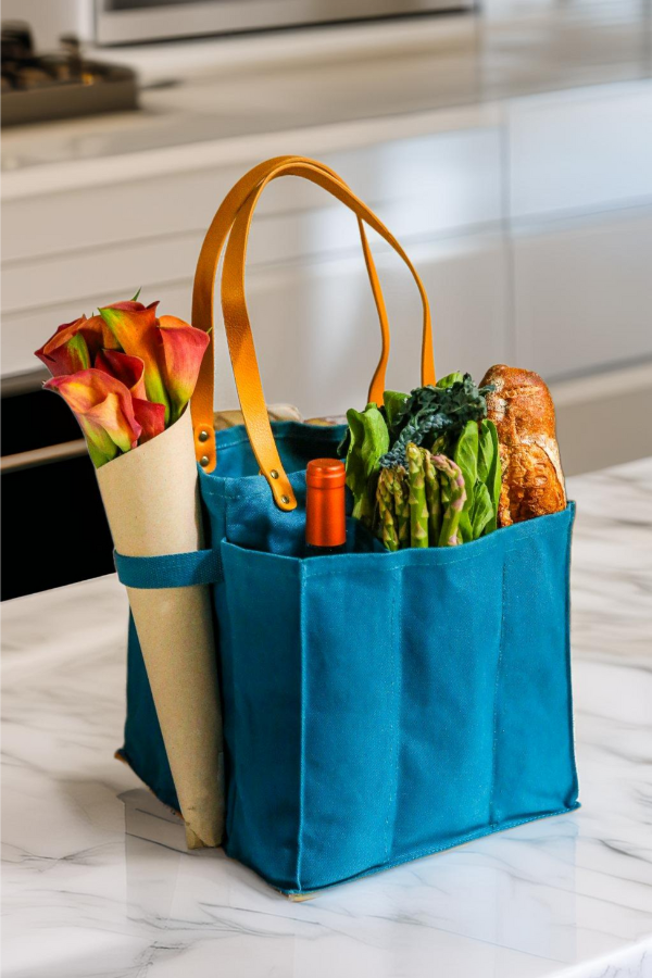 Petrol blue market tote with groceries and flowers on a kitchen counter.