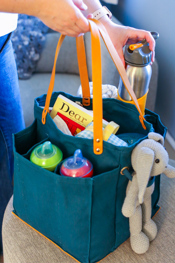 Petrol blue market tote with multiple pockets, holding water bottle, toys, and snacks, perfect for shopping and outings.