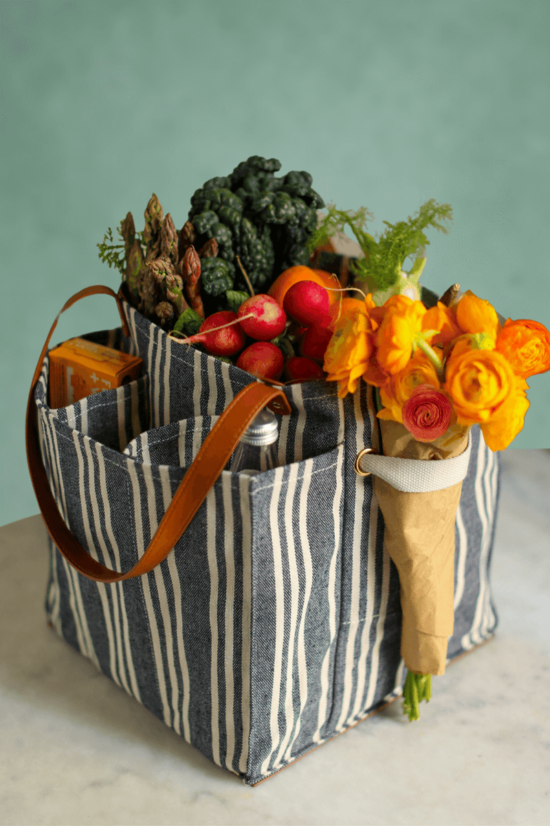 Striped market tote filled with fresh vegetables and flowers, showcasing its spacious pockets and stylish design.