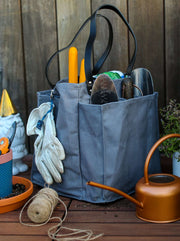 Grey multi-pocketed market tote filled with gardening tools and gloves, set on a wooden table.