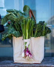 Natural canvas market tote filled with fresh vegetables like scallions and greens, showcasing its multi-pocket design.