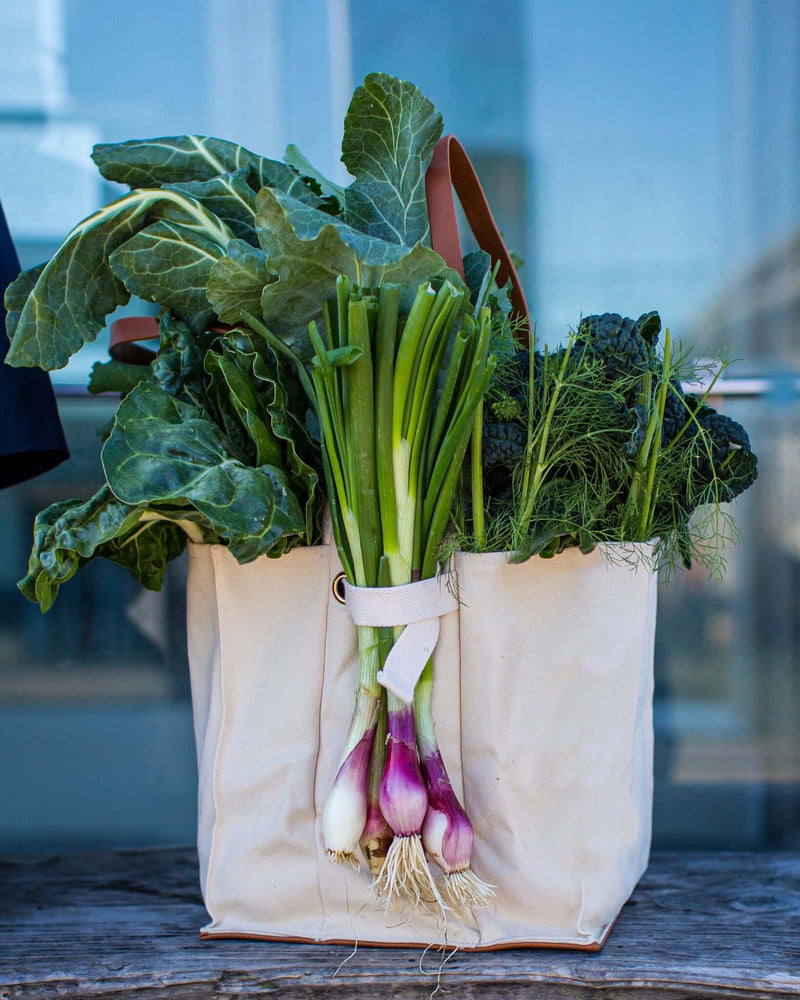 Natural canvas market tote filled with fresh vegetables like scallions and greens, showcasing its multi-pocket design.