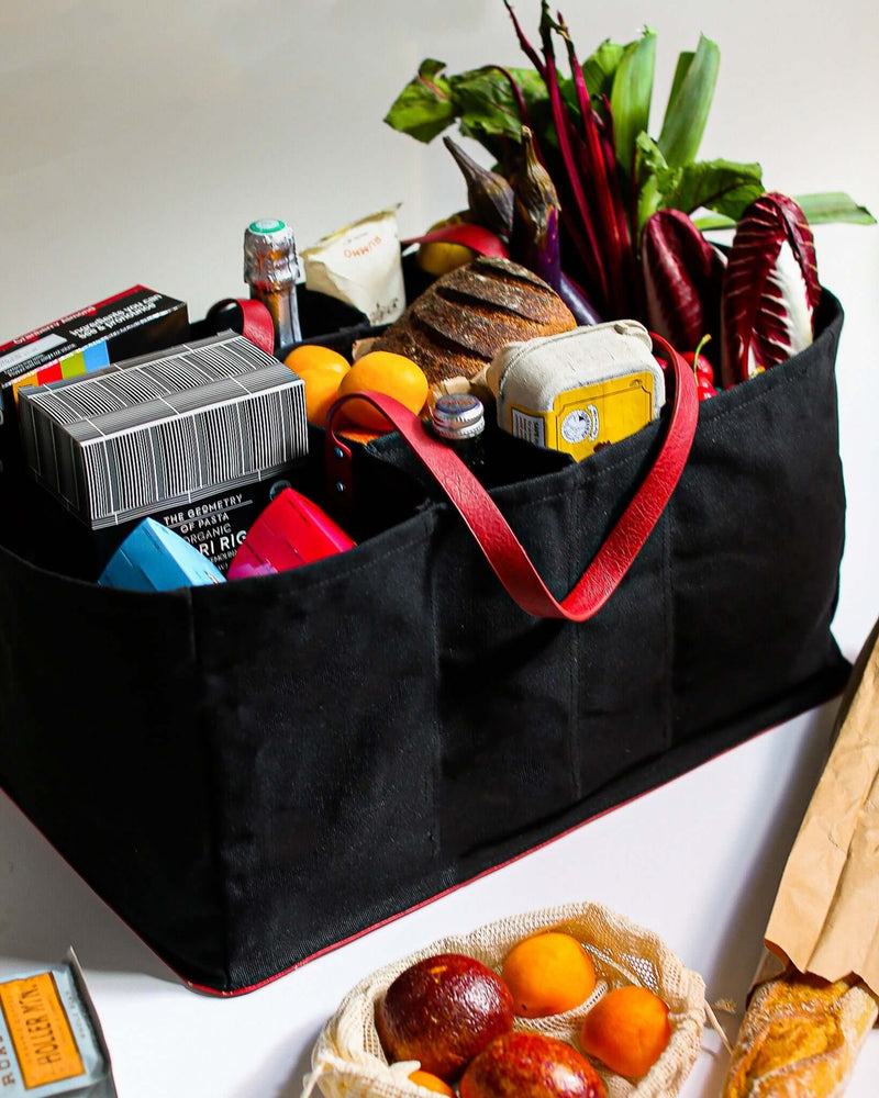 A black eco-friendly grocery tote filled with fresh produce, bread, and pantry items on a white surface.