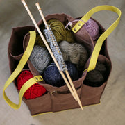 Brown tote bag filled with colorful yarn skeins and knitting needles for crafting projects.
